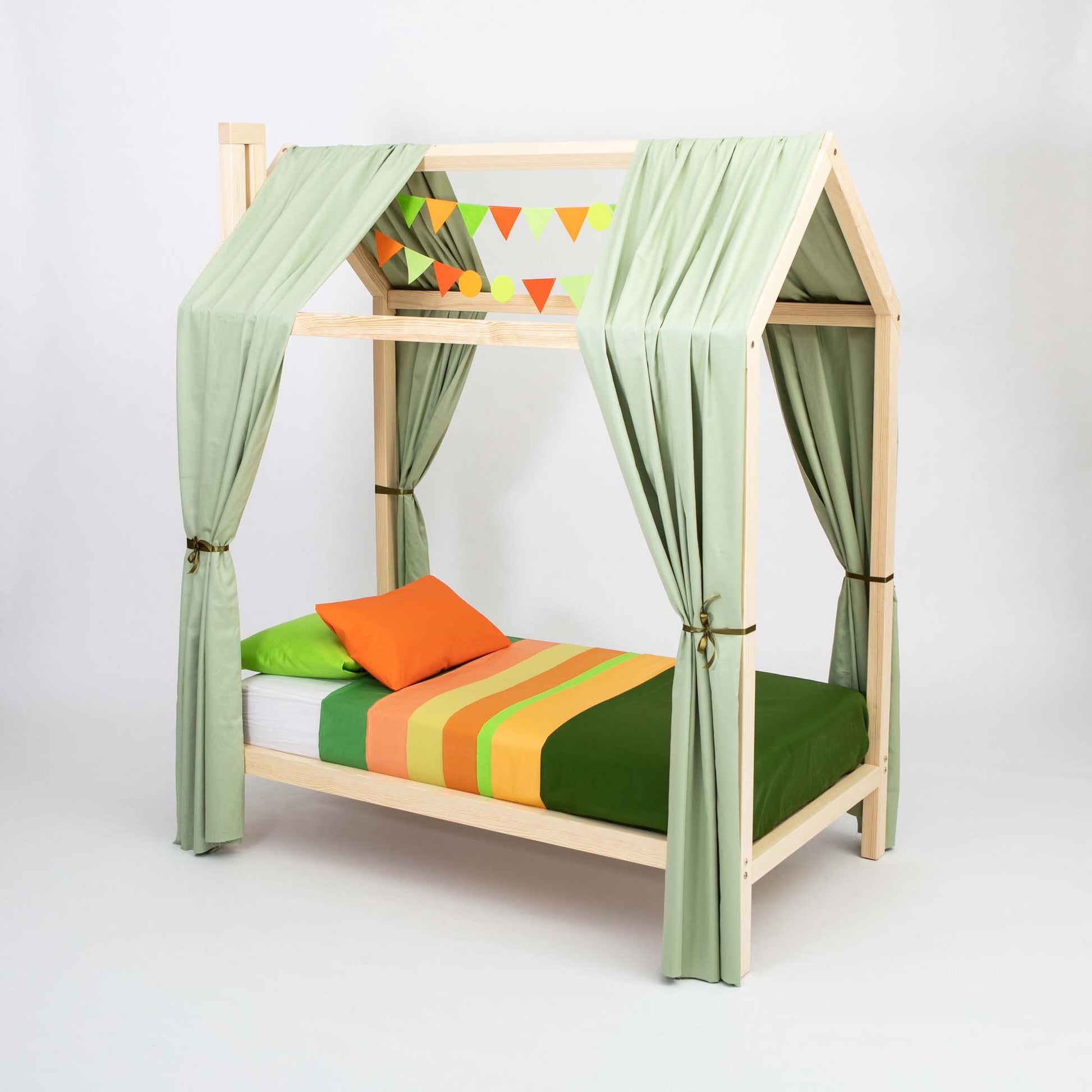 The Wooden House Bed on Legs is designed with a house-shaped canopy, adorned with green curtains, triangular colorful flag decorations, and bedding in green, orange, and yellow hues. This Montessori House Bed creates a cozy sleeping space for your child.