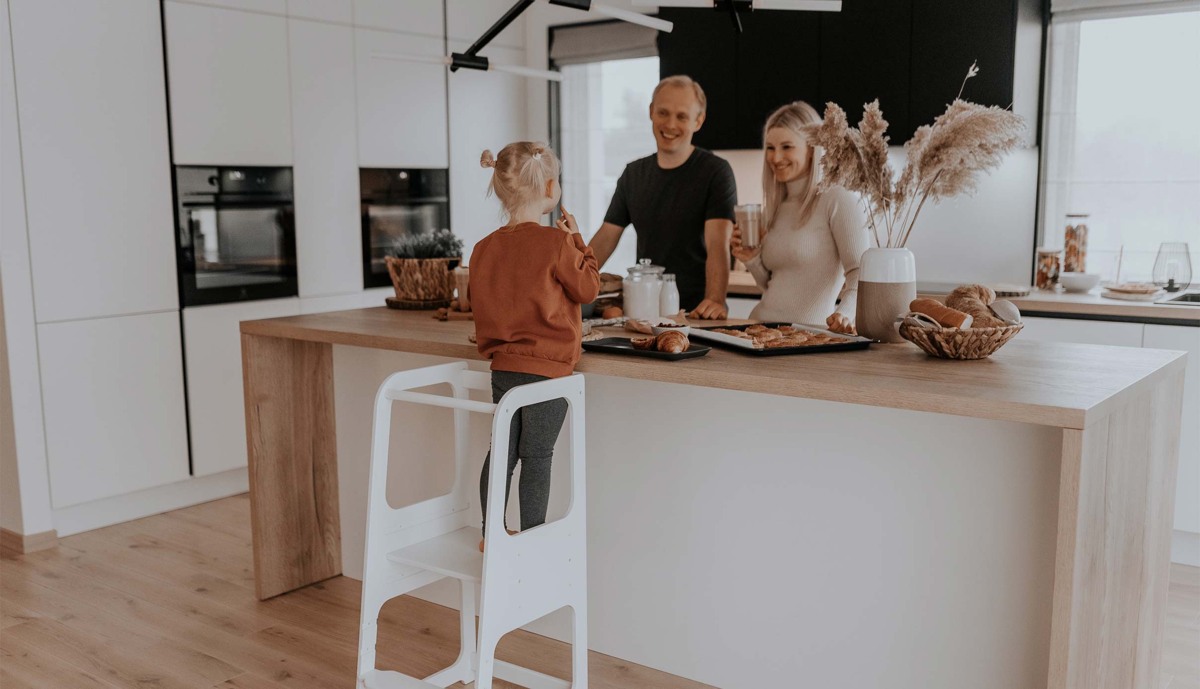 A family in a kitchen with a child on a step stool.
