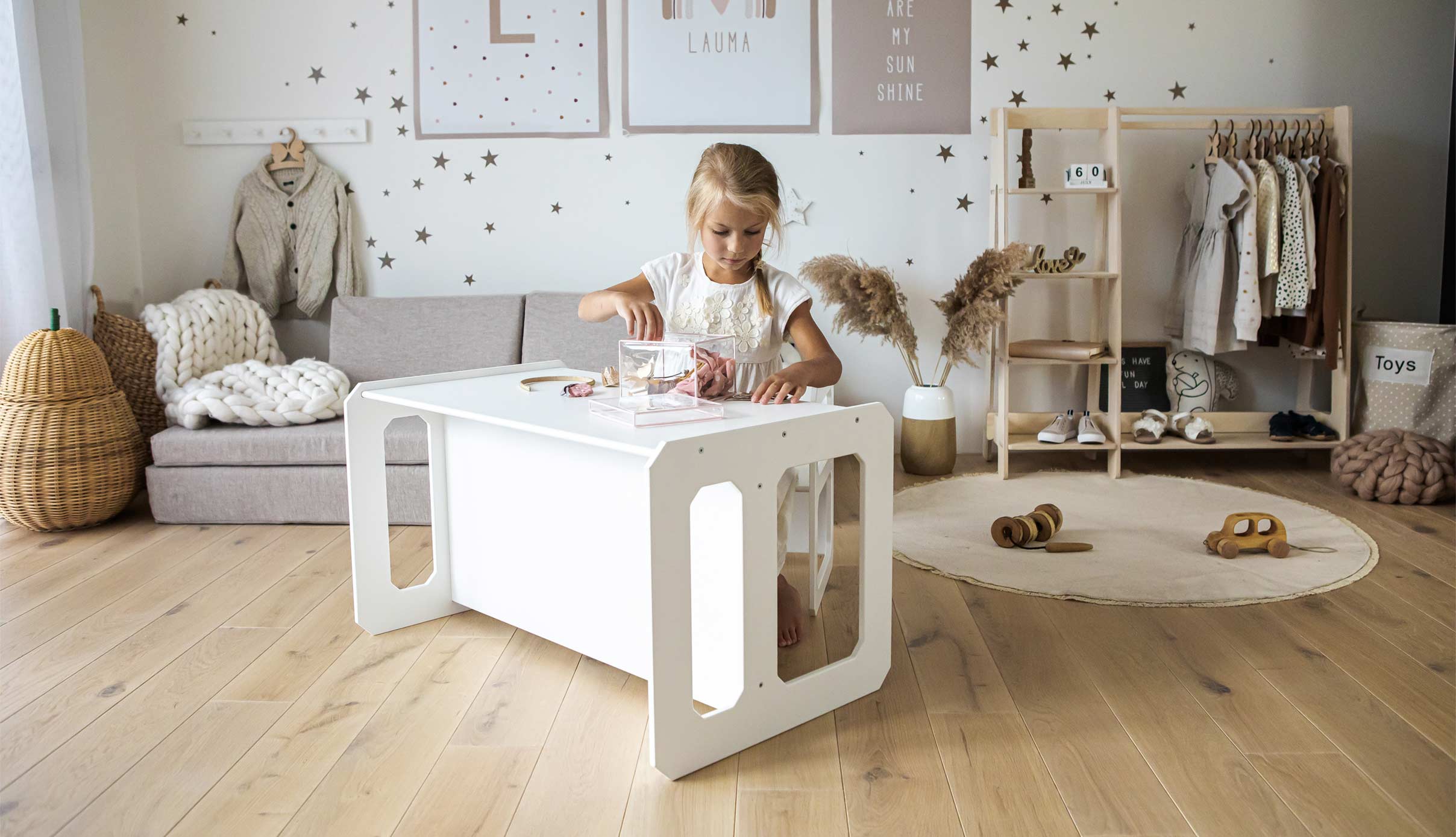 A little girl playing with a white table in a room.