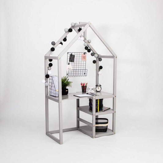 The House-shaped toddler desk offers a minimalist design that combines built-in storage, shelves, a clock, a plant, black and white string lights, and wall-mounted storage grids filled with papers and office supplies—perfect for creating an organized study space.
