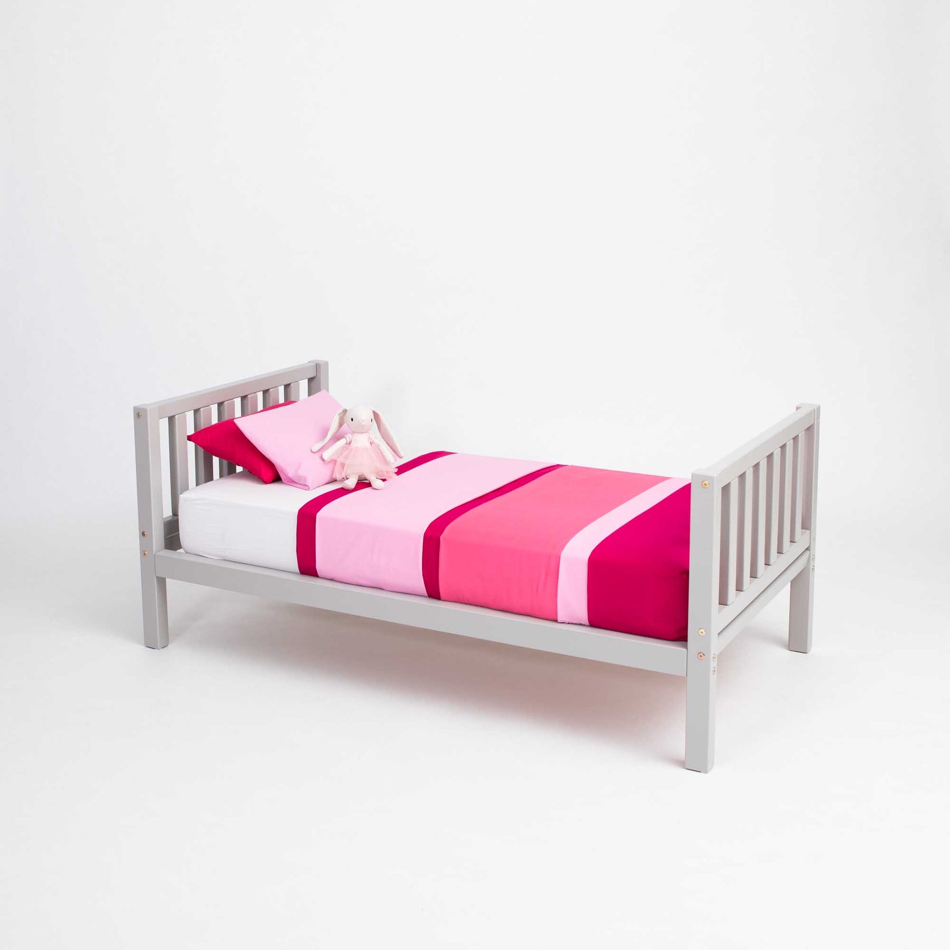 A Sweet Home From Wood raised kids' bed on legs with a headboard and footboard, with pink and white bedding, promoting independence.