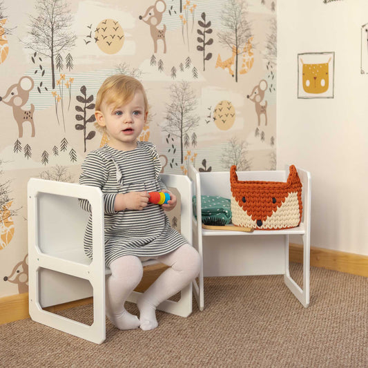 A little girl sitting on a Sweet Home From Wood Montessori weaning chair in a room.