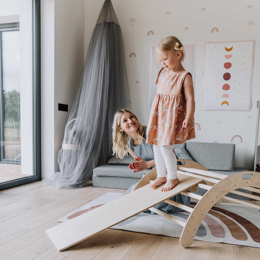 A little girl is playing on a Sweet Home From Wood climbing arch, kids' indoor gym in the living room.