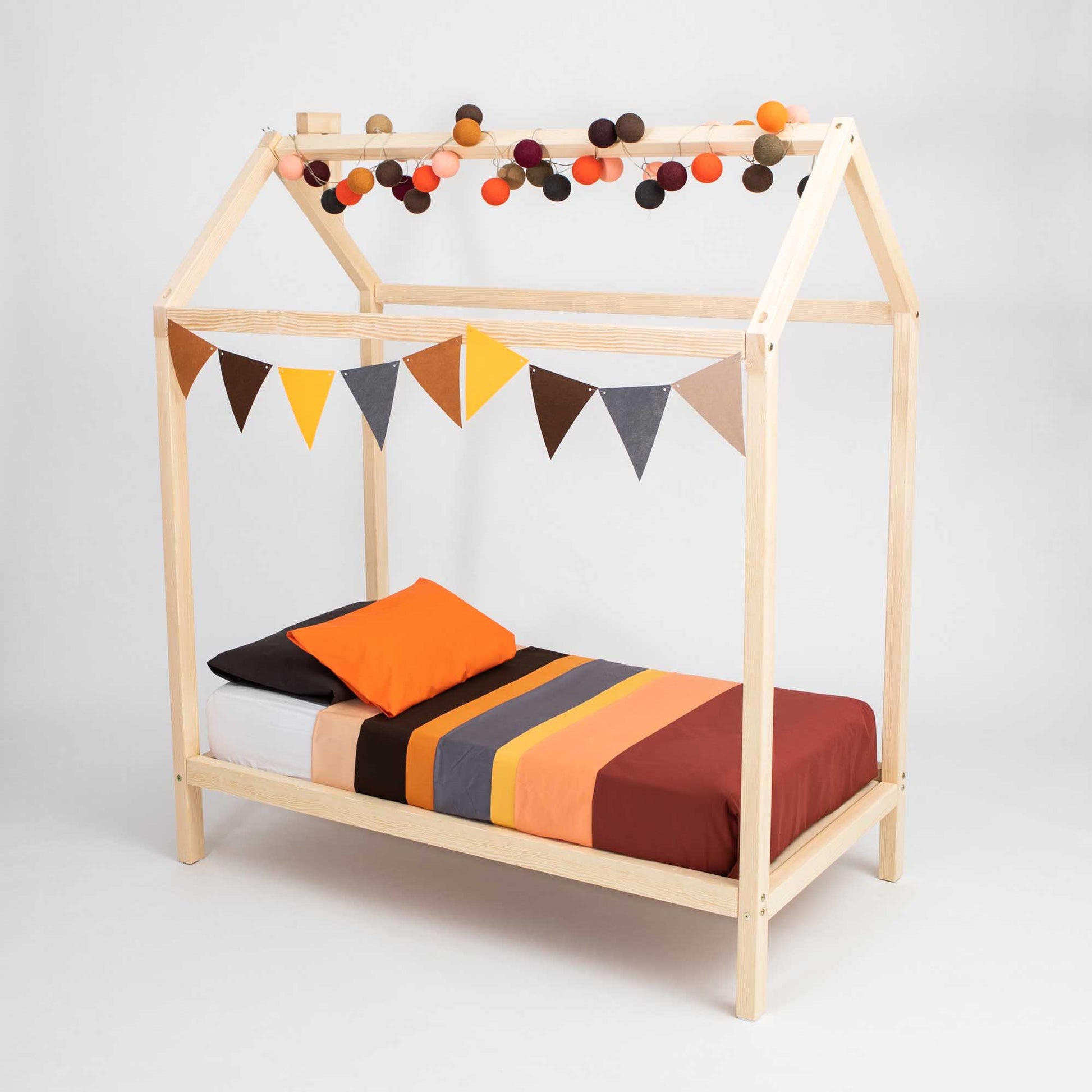 A wooden house bed on legs with bunting and pom poms.