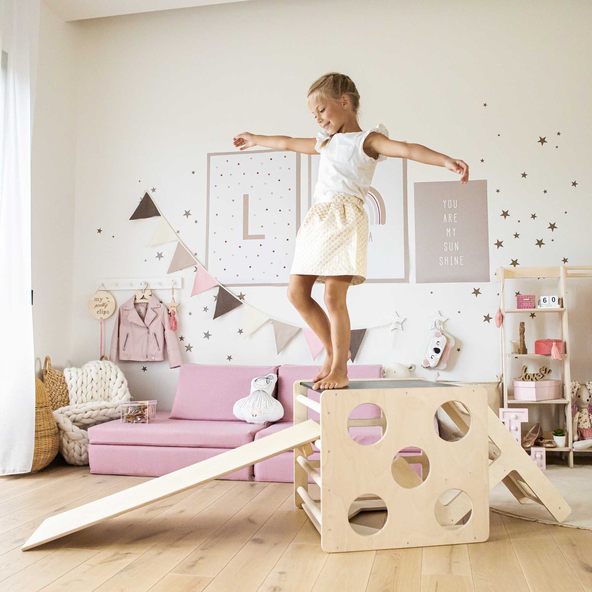 A little girl sitting on a Transformable climbing cube / table and chair and a ramp in a playoom.