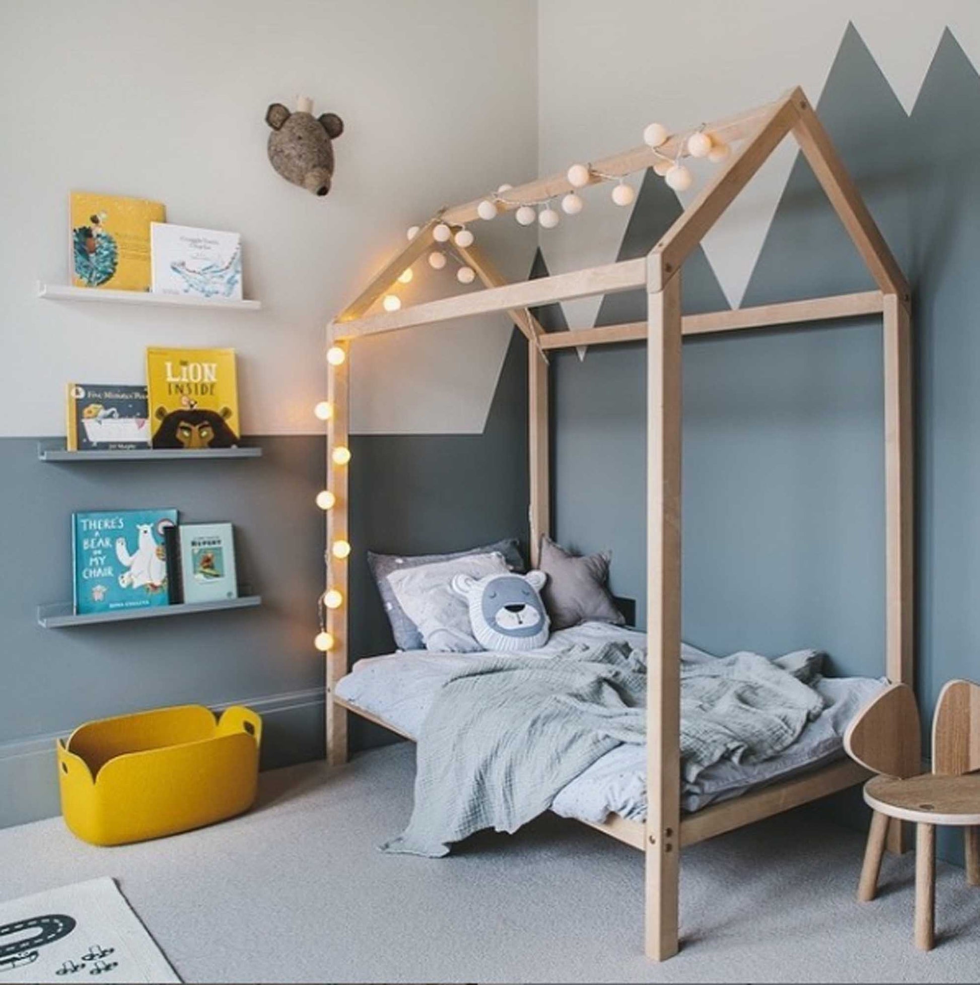 A wooden house bed on legs with books and a lamp in a boy's room.