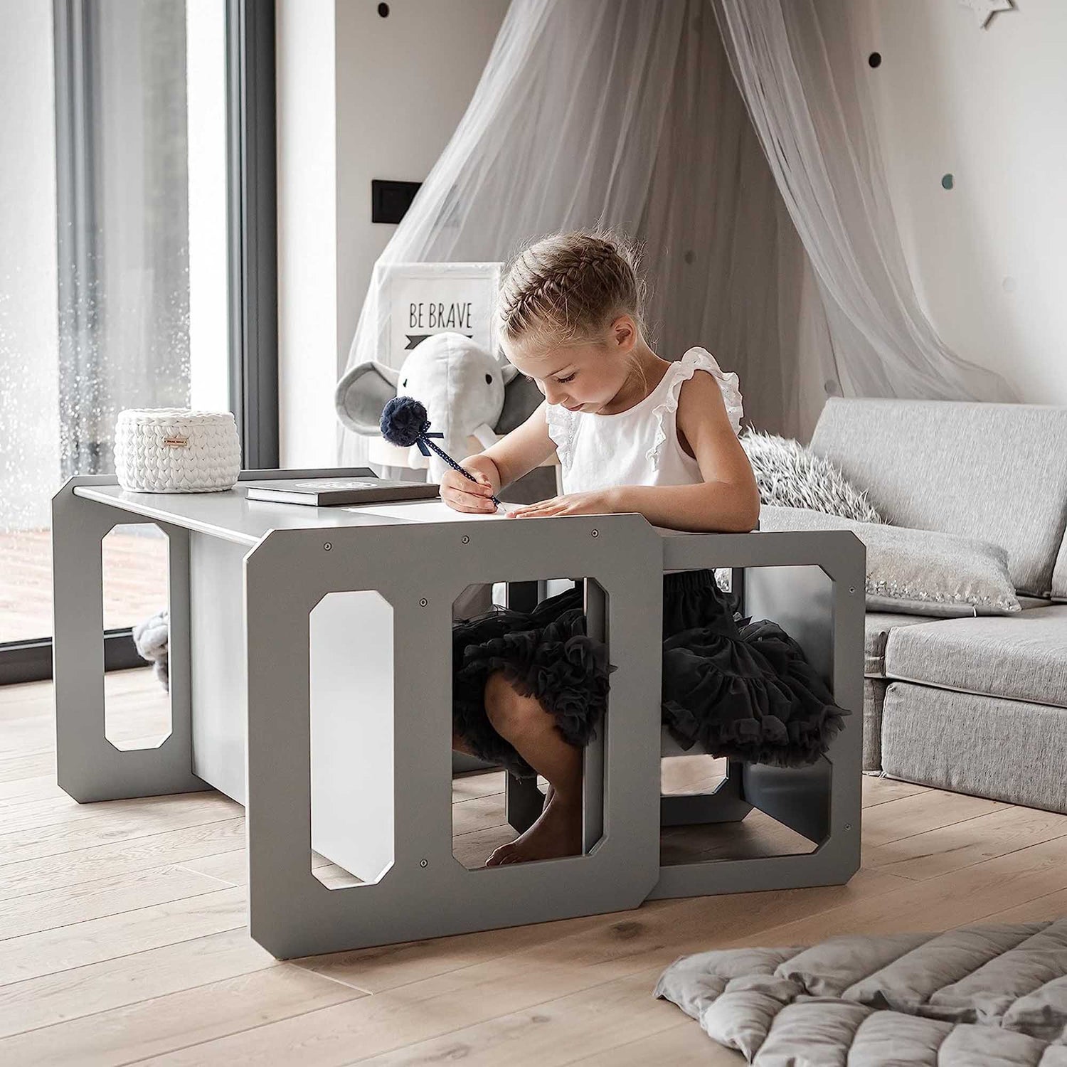 A little girl sitting at a Sweet Home From Wood Montessori weaning table and chair set in a room.