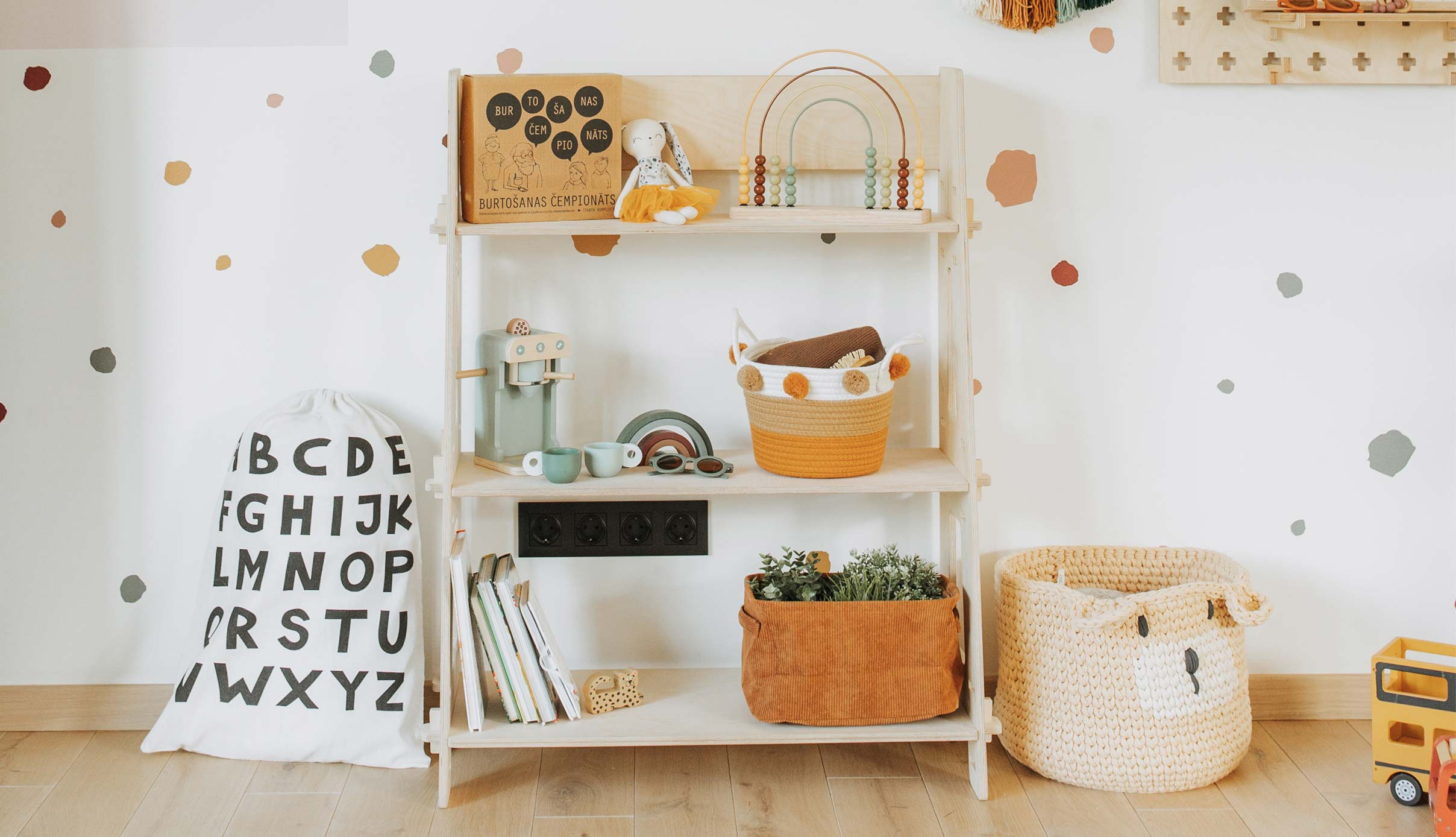 A child's room with a book shelf, toys and a polka dot wall.