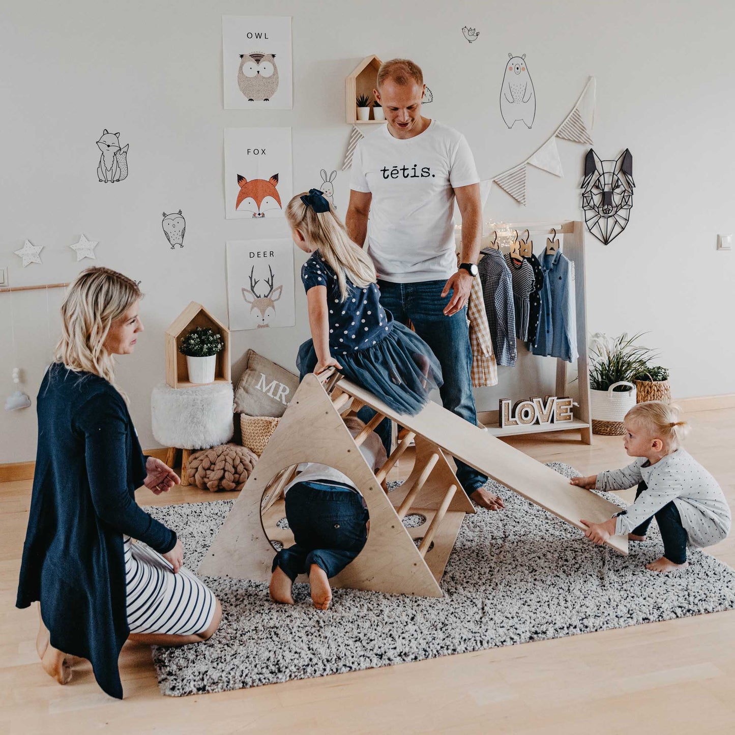 A family is playing with a climbing triangle with sensory panels in an indoor playroom.