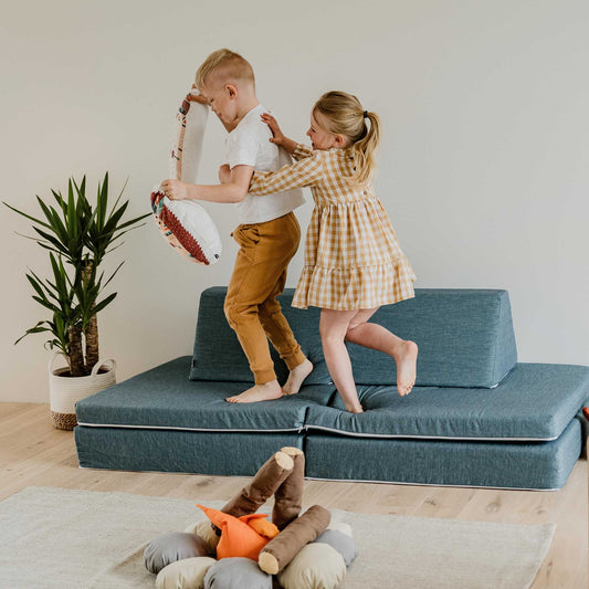 Two children playing on a Sweet HOME from wood activity play couch set in a living room.