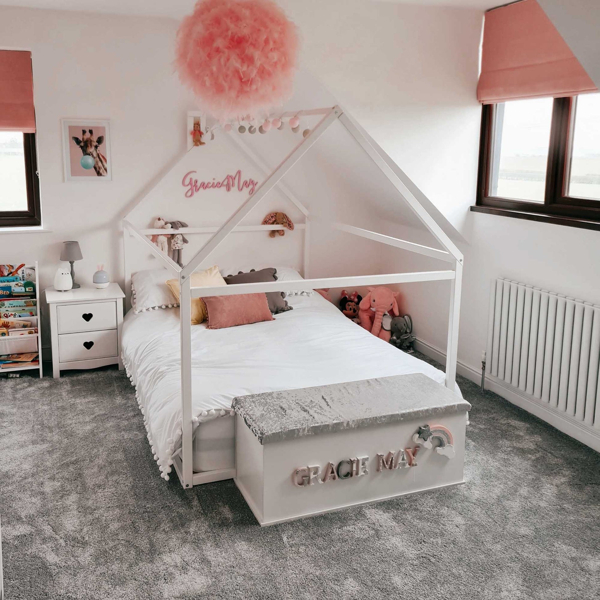 A cozy sleep haven adorned with pink pom poms, featuring a Sweet Home From Wood's Wooden zero-clearance house bed draped with a house-shaped canopy.