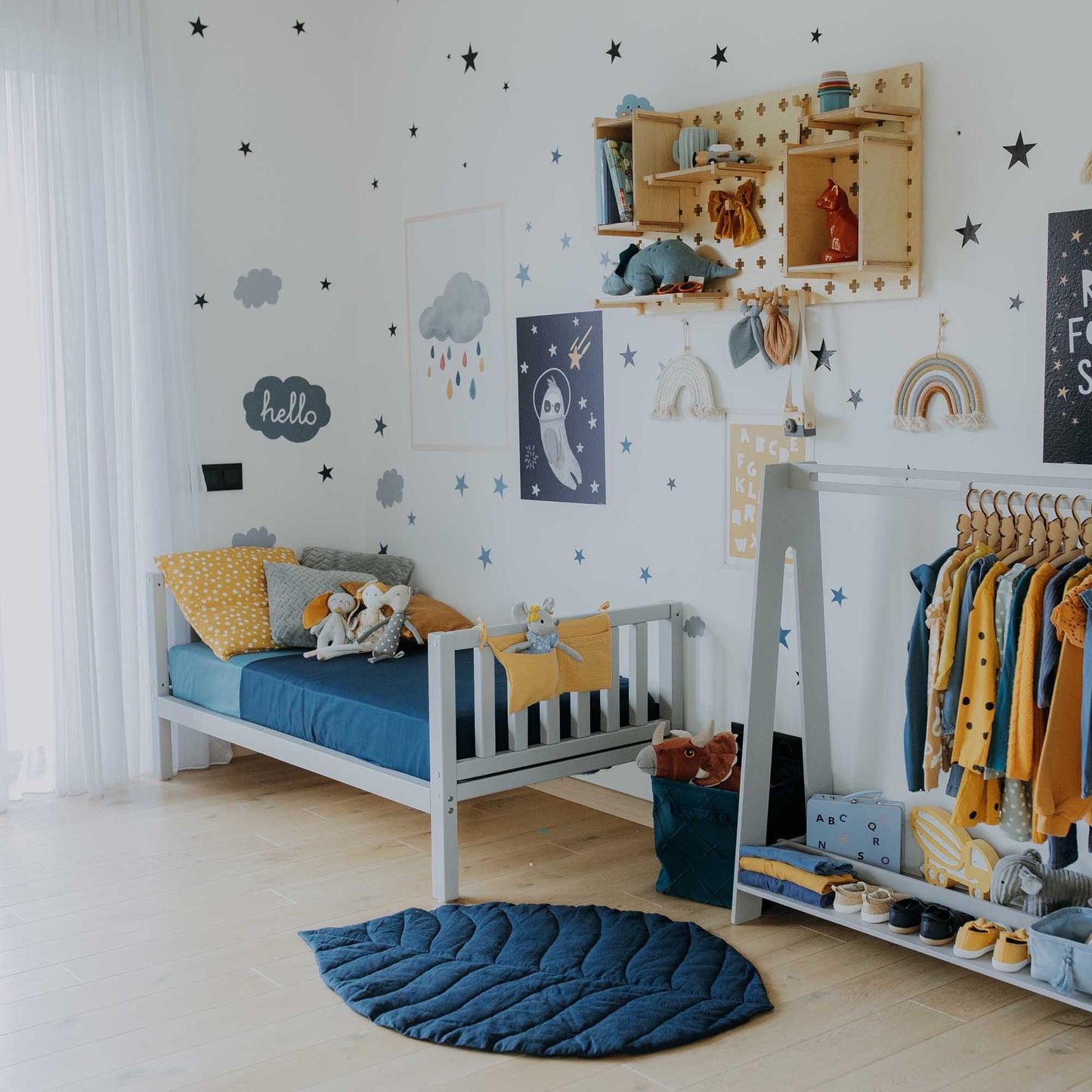 A Montessori-inspired child's room with blue and yellow decor featuring a Sweet Home From Wood raised kids' bed on legs with a headboard and footboard.