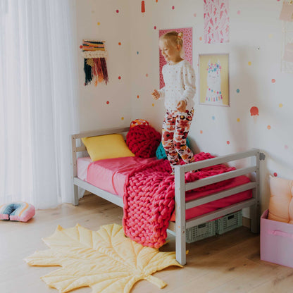 A toddler standing on a Sweet Home From Wood 2-in-1 transformable kids' bed with a 3-sided horizontal rail in a girl's room.