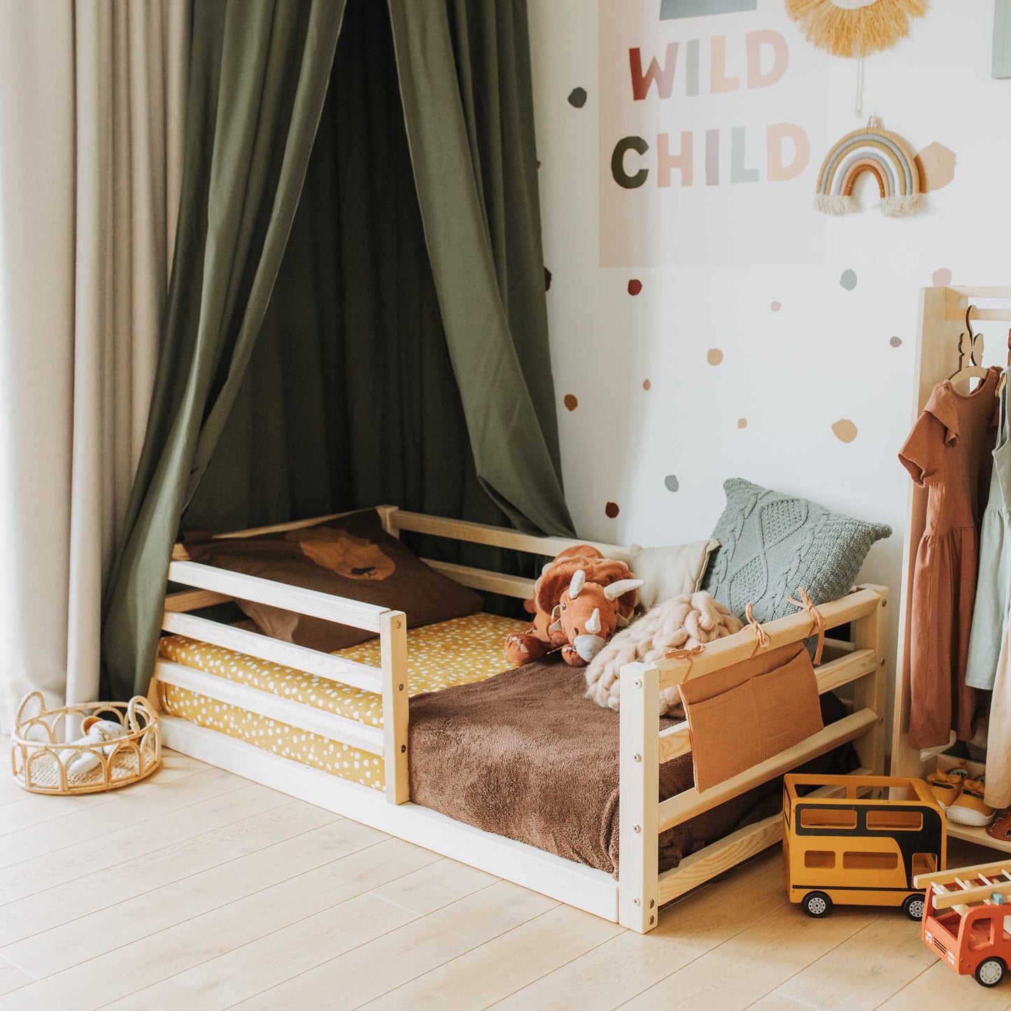 A child's room with an independent sleeping arrangement and a variety of toys includes the Sweet Home From Wood floor-level kids' bed with a horizontal rail fence.