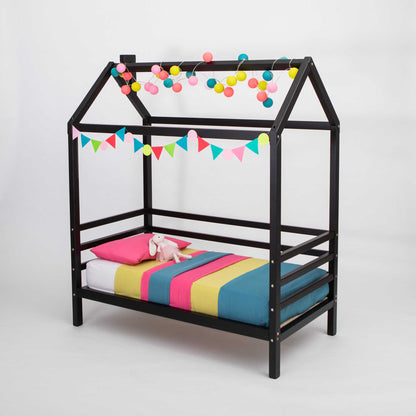A children's house bed on legs with 3-sided rails with a black frame and colorful bedding.
