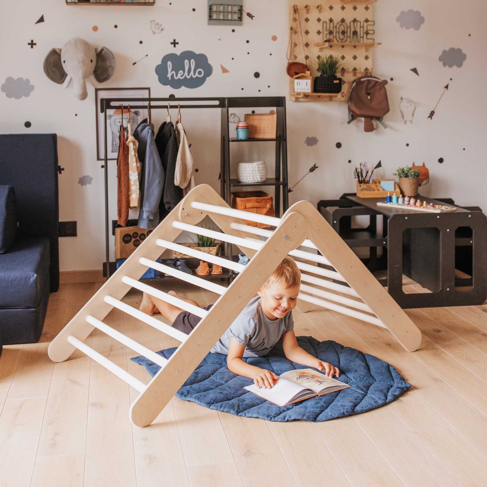 A child is playing in a room with a wooden play structure, specifically a Sweet Home From Wood Montessori climber which includes a climbing triangle, foldable climbing triangle, and a ramp.