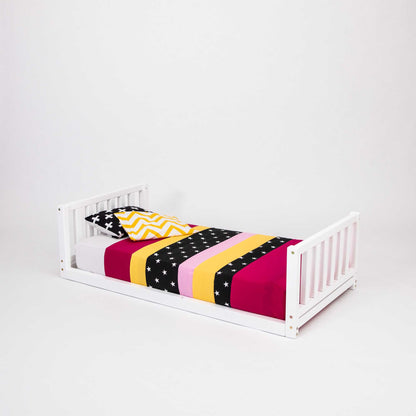 A 2-in-1 kid's bed on legs with a vertical rail headboard and footboard made of solid pine or birch wood, topped with a striped blanket.