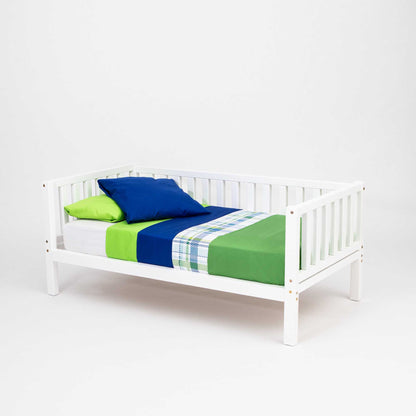 A children's platform bed on legs with 3-sided rails, with Montessori-inspired green and blue bedding.