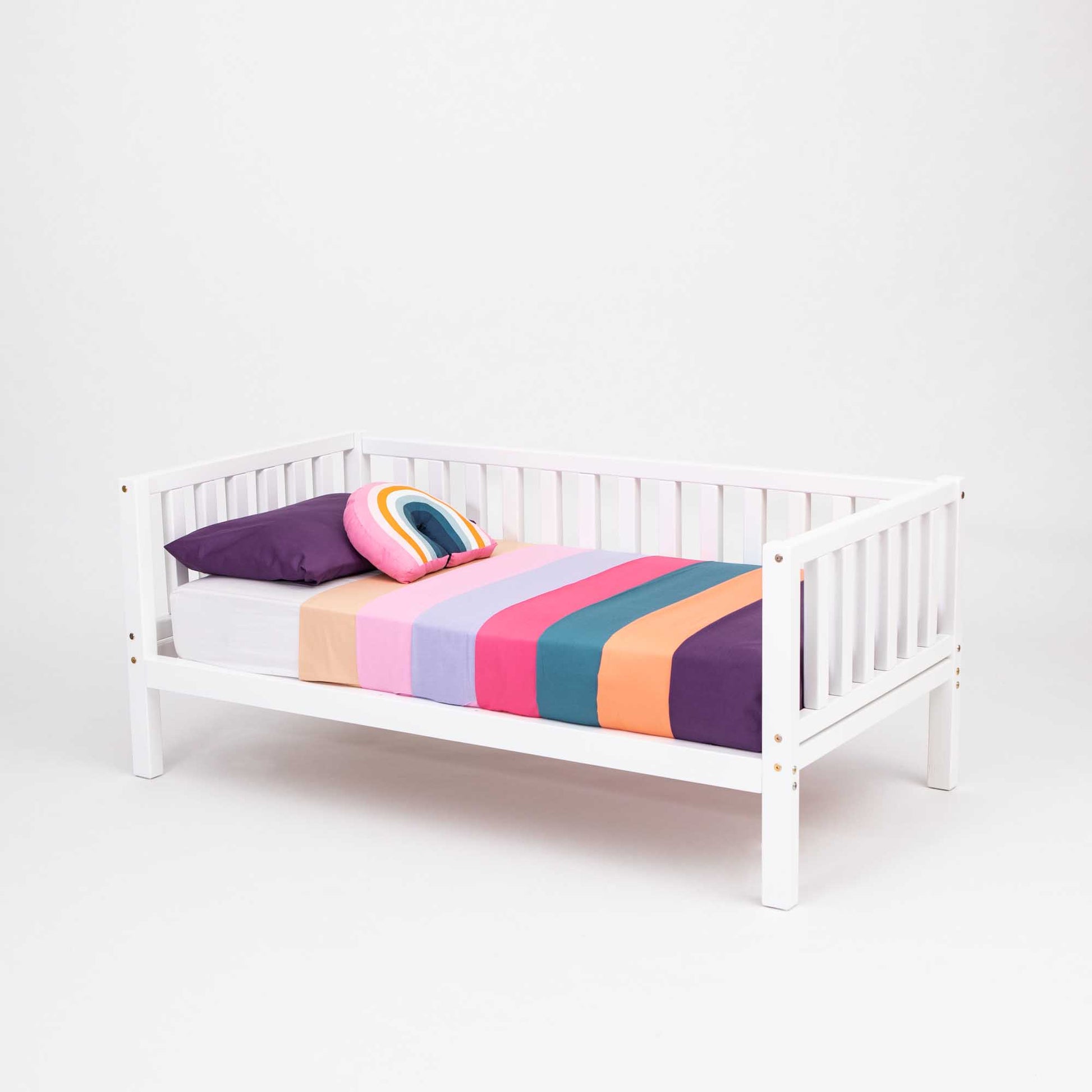 A vibrant and playful 2-in-1 children's bed adorned with a colorful striped blanket. (Product Name: 2-in-1 toddler bed on legs with a 3-sided vertical rail) from (Brand Name: Sweet Home From Wood).