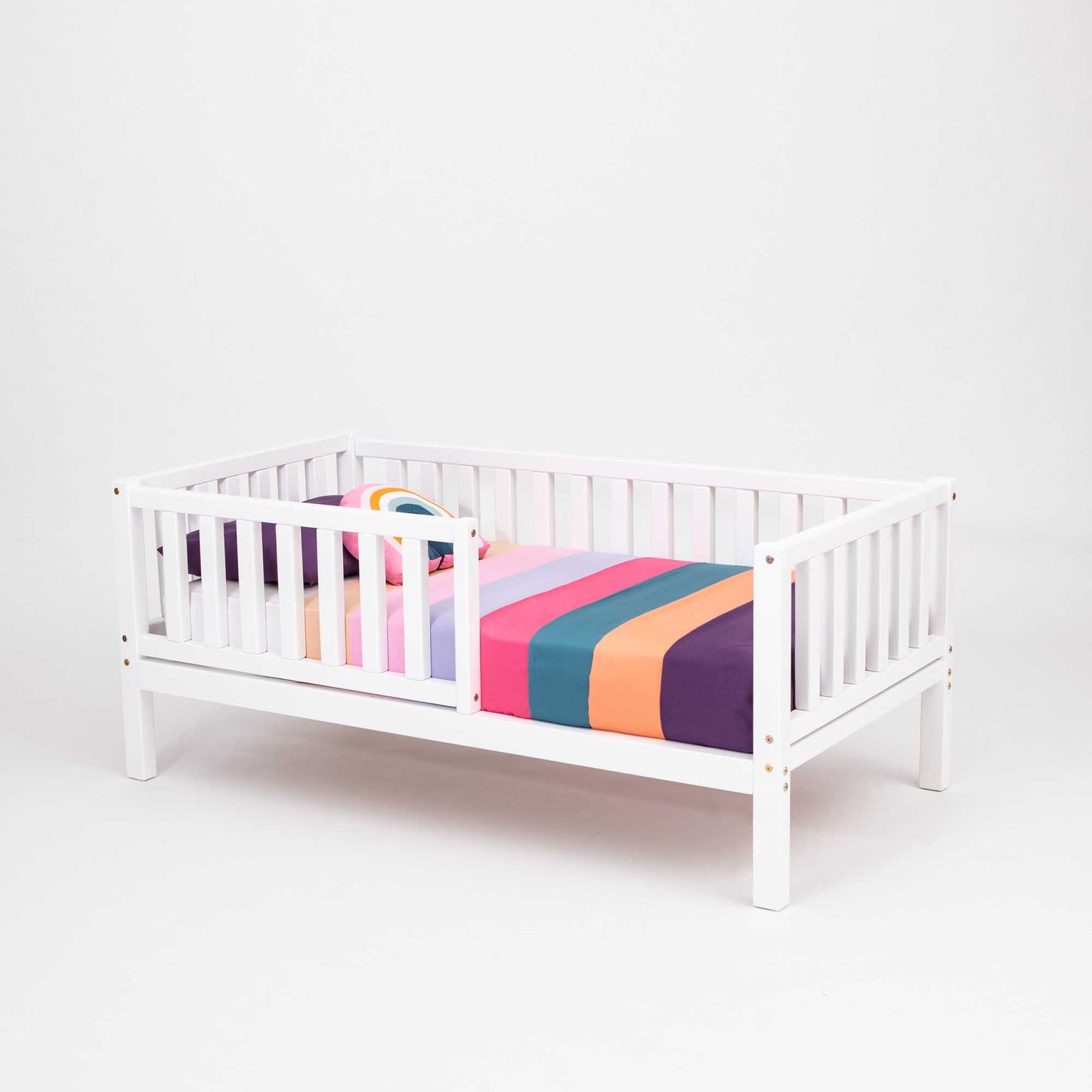 A Sweet Home From Wood 2-in-1 toddler bed on legs with a vertical rail fence with a colorful striped sheet made of solid pine, ensuring long-lasting durability.