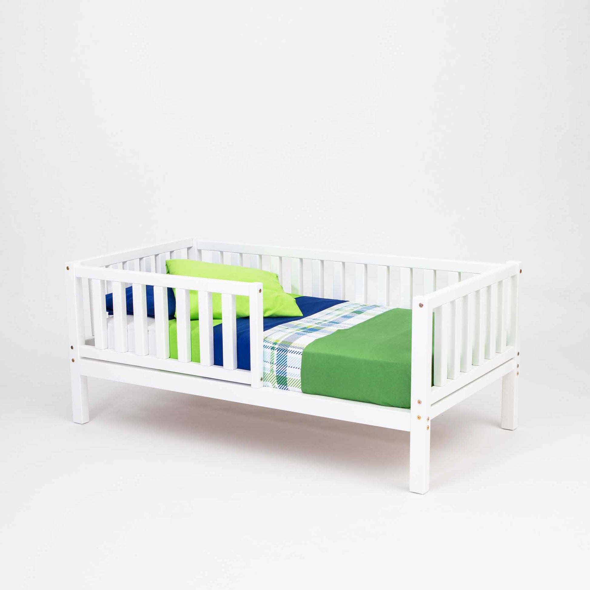 A long-lasting, 2-in-1 toddler bed on legs with a vertical rail fence made of solid pine with white frame and green and blue bedding from Sweet Home From Wood.