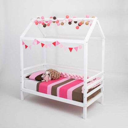 A Children's house bed on legs with 3-sided rails with a pink and white striped blanket.
