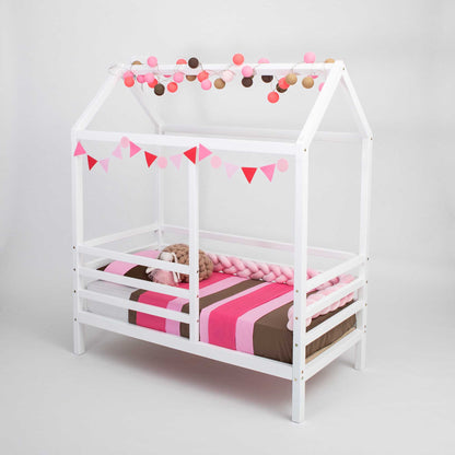 A wooden house bed on legs with a fence and a pink and white striped blanket.