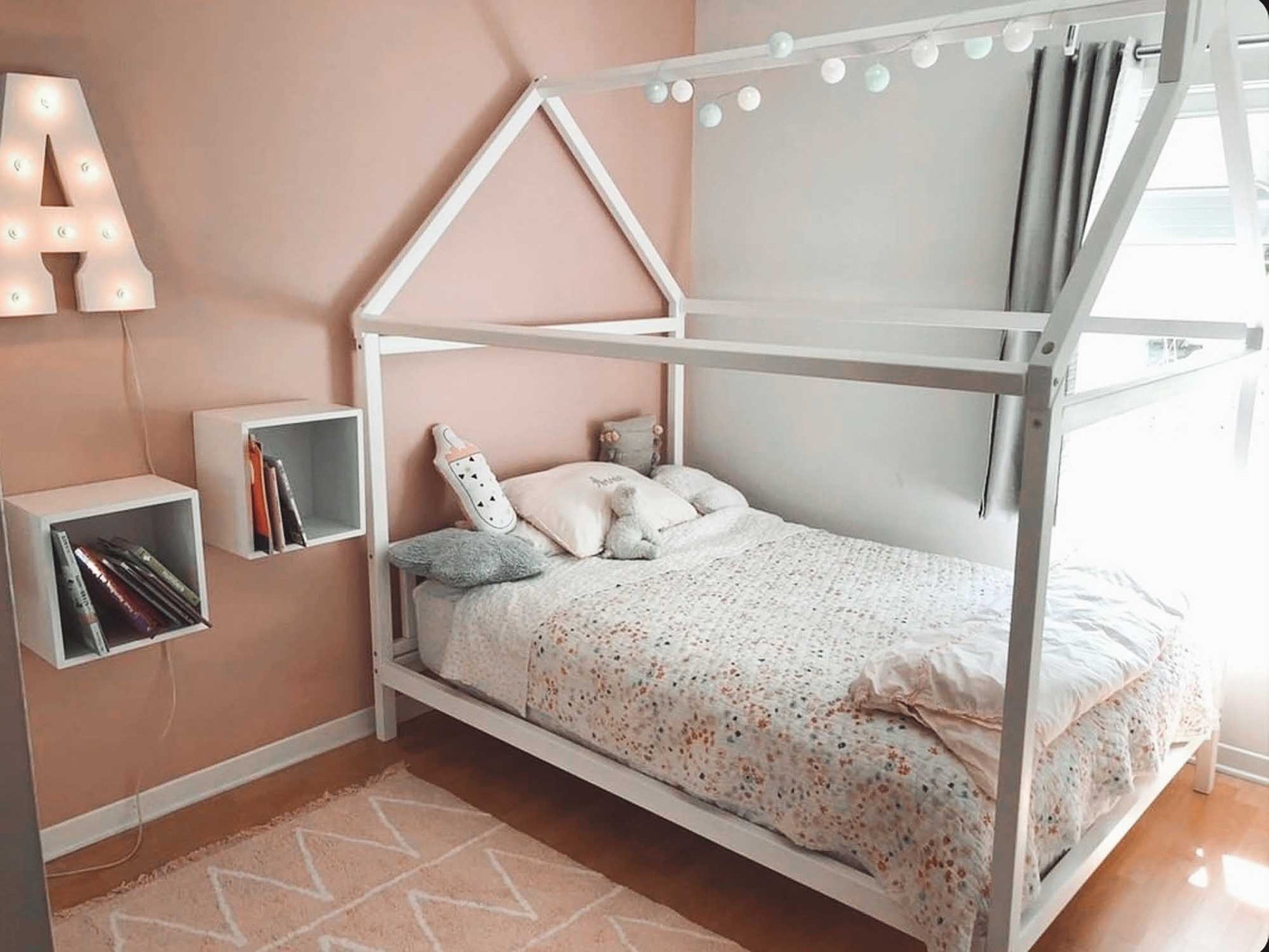A girl's bedroom with pink walls and a toddlers' house bed on legs with a headboard.