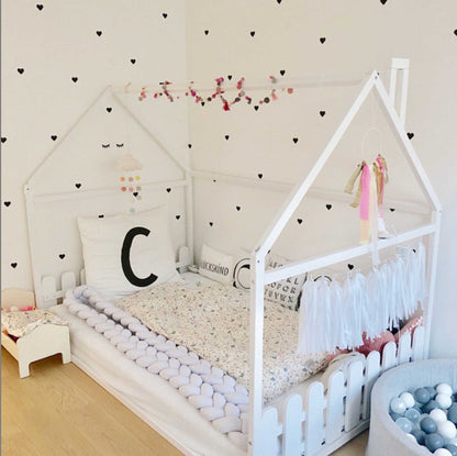A girl's room with a floor house-frame bed with 3-sided picket fence rails and a heart wall decal.