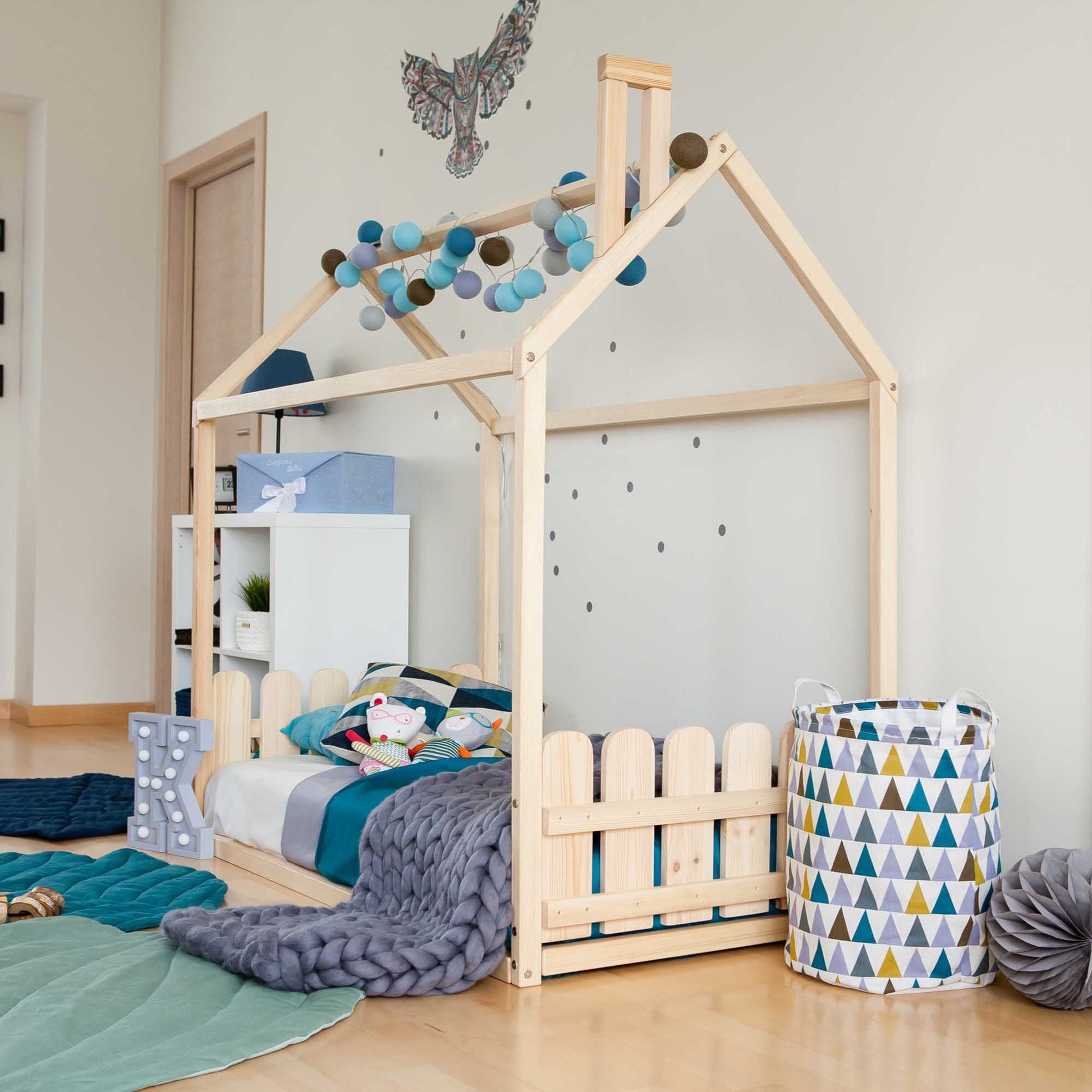 A child's bedroom with a Montessori house-frame bed with a picket fence headboard and footboard.