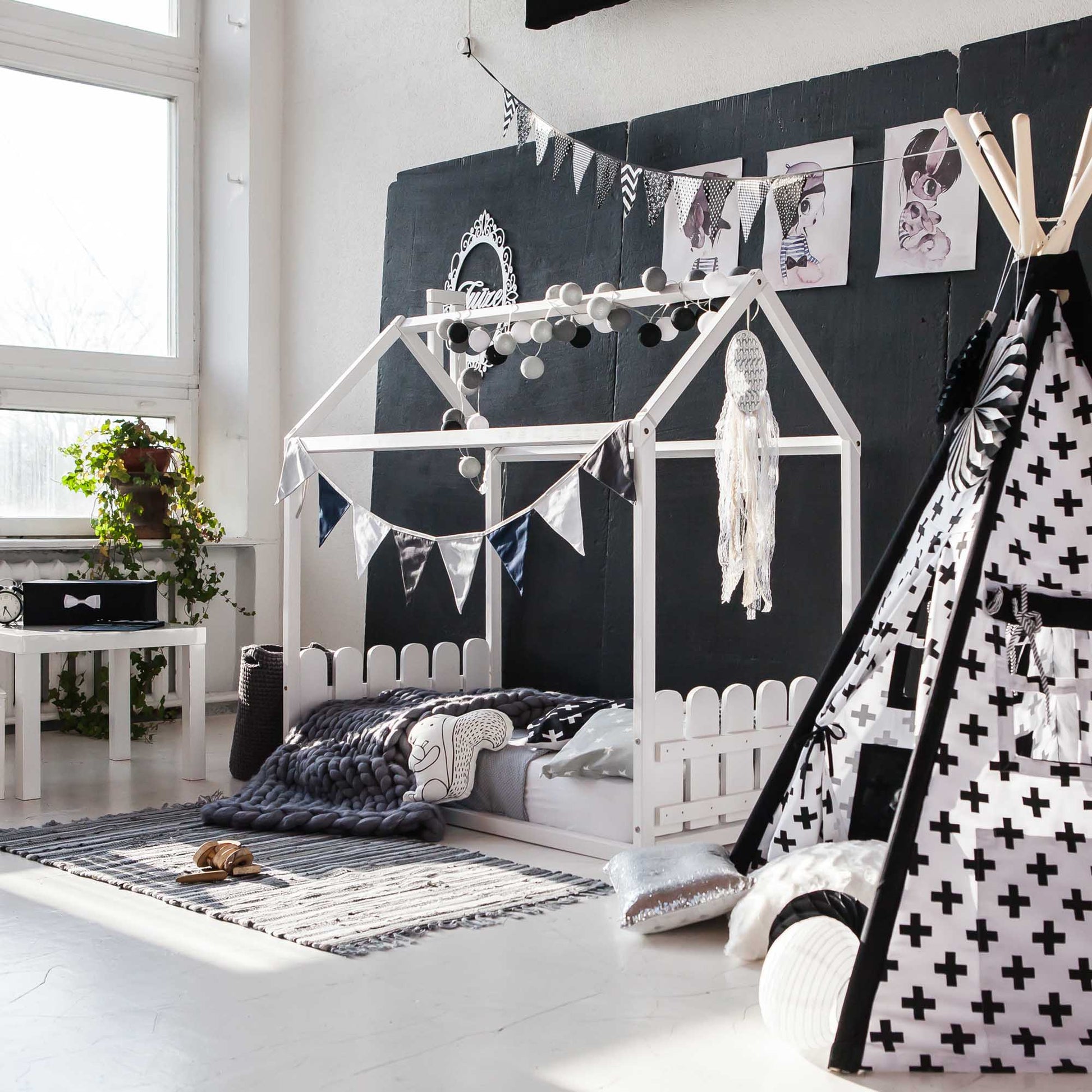 A black and white kids room with a teepee bed featuring a Montessori house-frame bed with a picket fence headboard and footboard for toddlers.