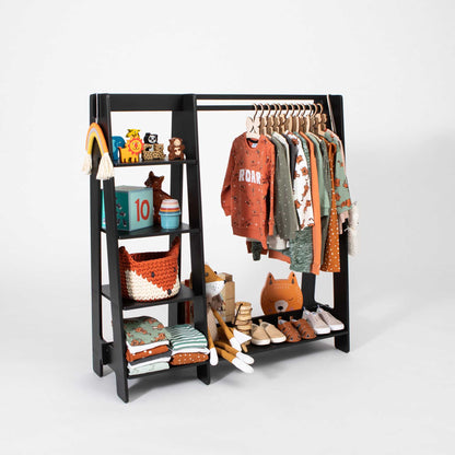 A Sweet Home From Wood Montessori-inspired children's wardrobe featuring a black dress up clothing rack with clothes and toys neatly arranged on storage shelves.