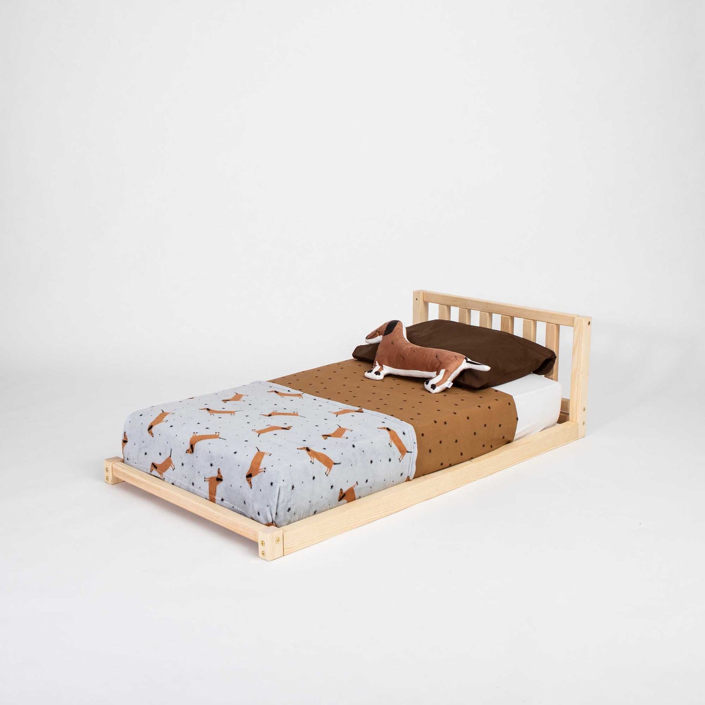A Sweet Home From Wood 2-in-1 toddler bed on legs with a vertical rail headboard, made of solid pine or birch wood, with a dog resting on it.