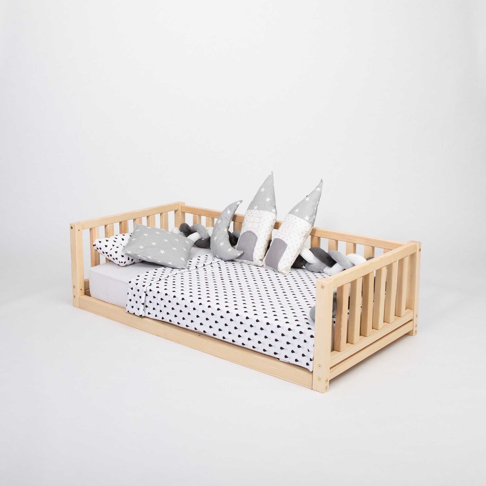 This 2-in-1 toddler bed on legs with a 3-sided vertical rail from Sweet Home From Wood features polka dot pillows and a wooden frame made of solid pine or birch wood. It is designed as a floor-level bed for toddlers.