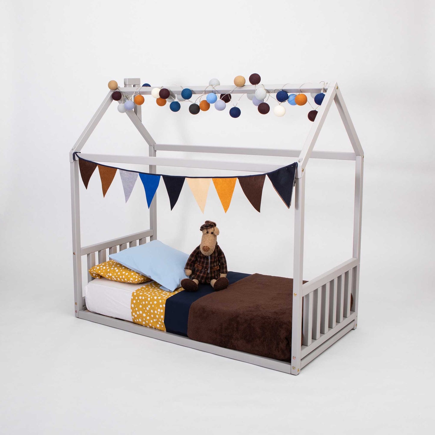 A Sweet Home From Wood toddler house bed with a headboard and footboard, creating a cozy sleep haven adorned with bunting and stuffed animals.