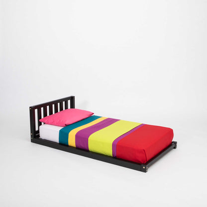 A colorful striped sheet on a Sweet Home From Wood 2-in-1 toddler bed on legs with a vertical rail headboard.