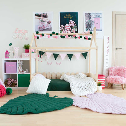 A girl's room with a floor house-frame bed with 3-sided picket fence rails and pink and green decorations.