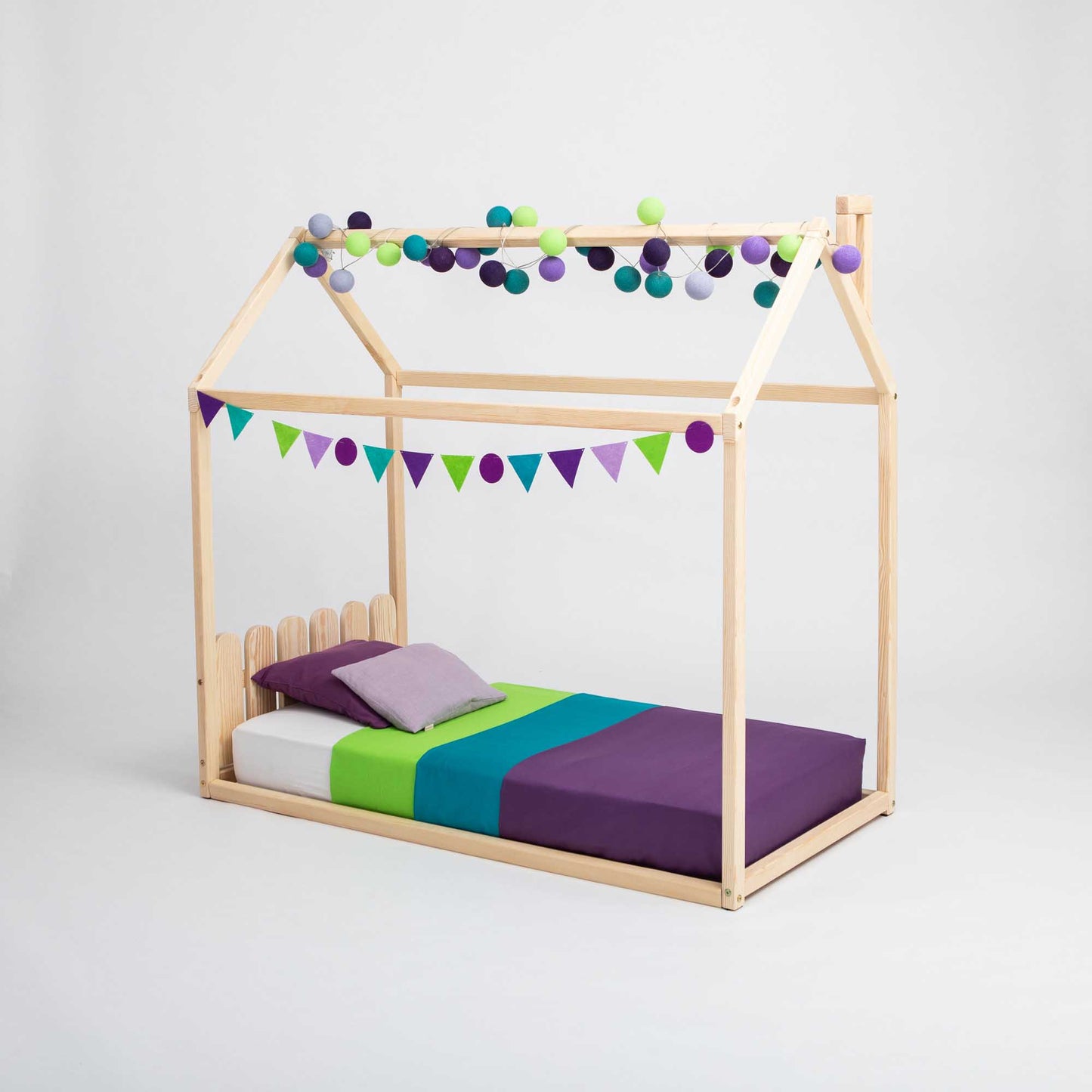 A child's wooden Kids' house-frame bed with a picket fence headboard, designed in a montessori house bed style.