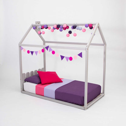 A Kids' house-frame bed with a picket fence headboard for toddlers with a pink and purple canopy and pom poms.