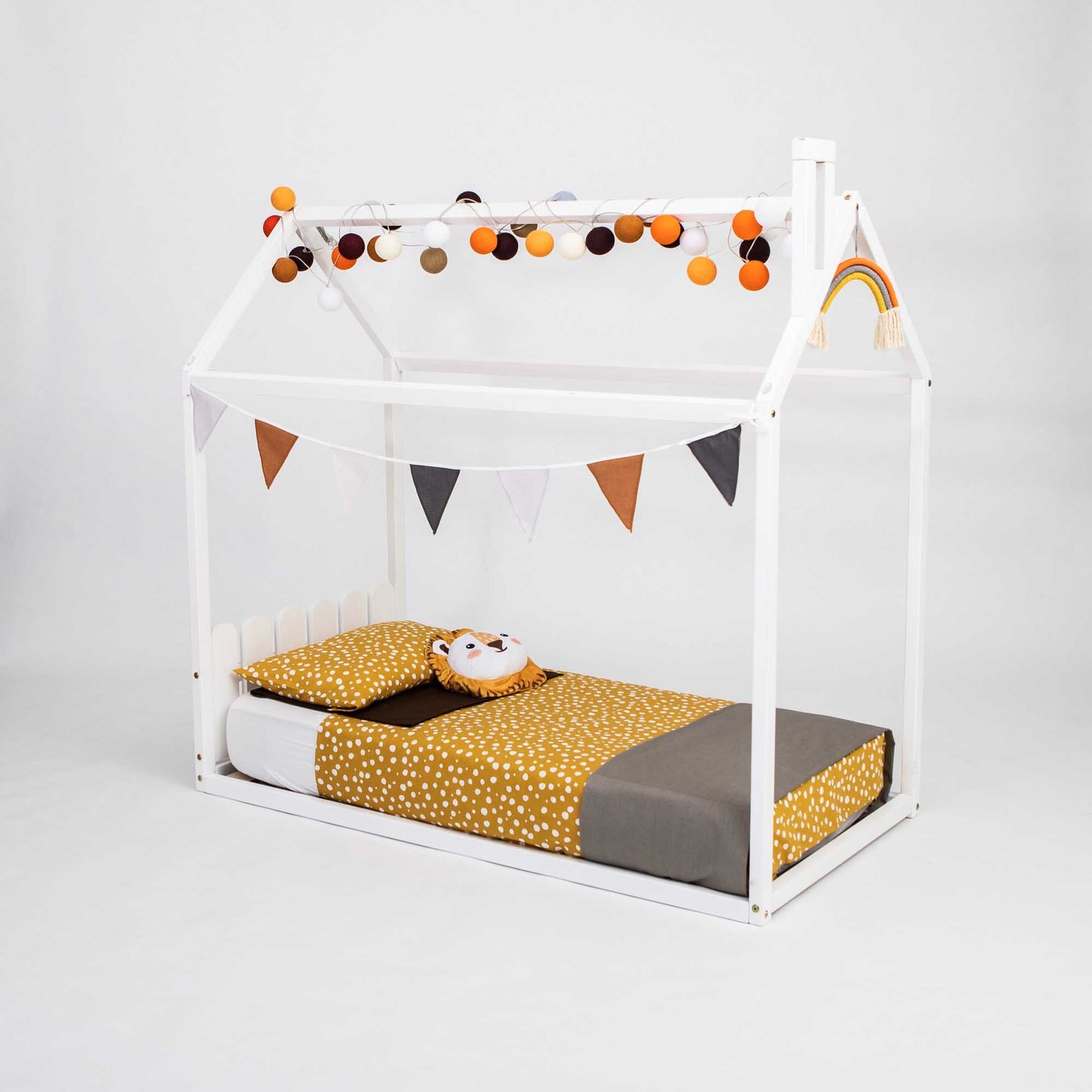 A kids' house-frame bed with a picket fence headboard decorated with bunting and pom poms.