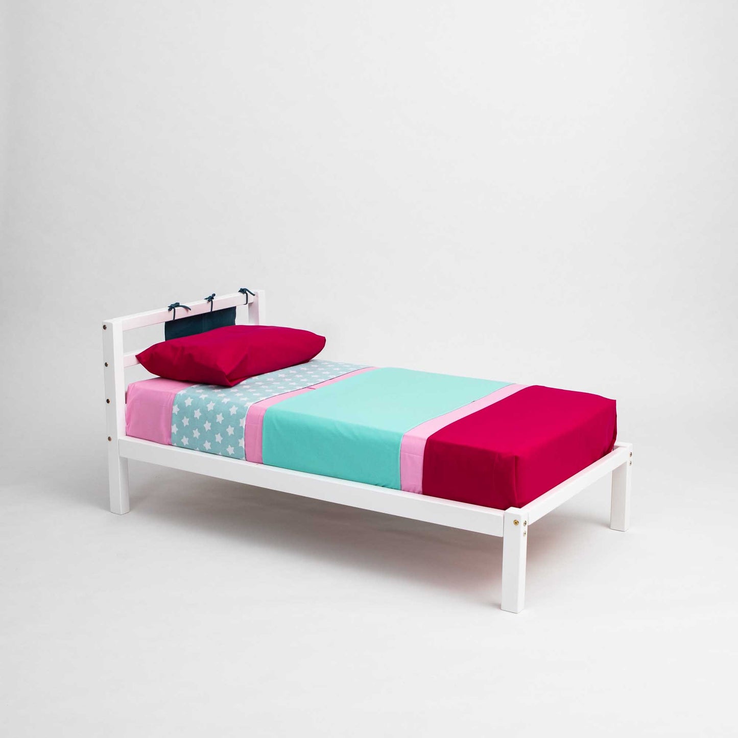 A Sweet Home From Wood 2-in-1 transformable kids' bed with a horizontal rail headboard, with a pink, blue, and green cover suitable for girls.