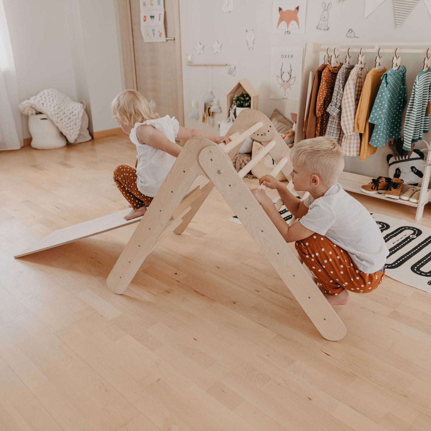 Two children using the Foldable climbing triangle with 2 slope levels to play with a wooden toy and develop their motor skills in a room.
