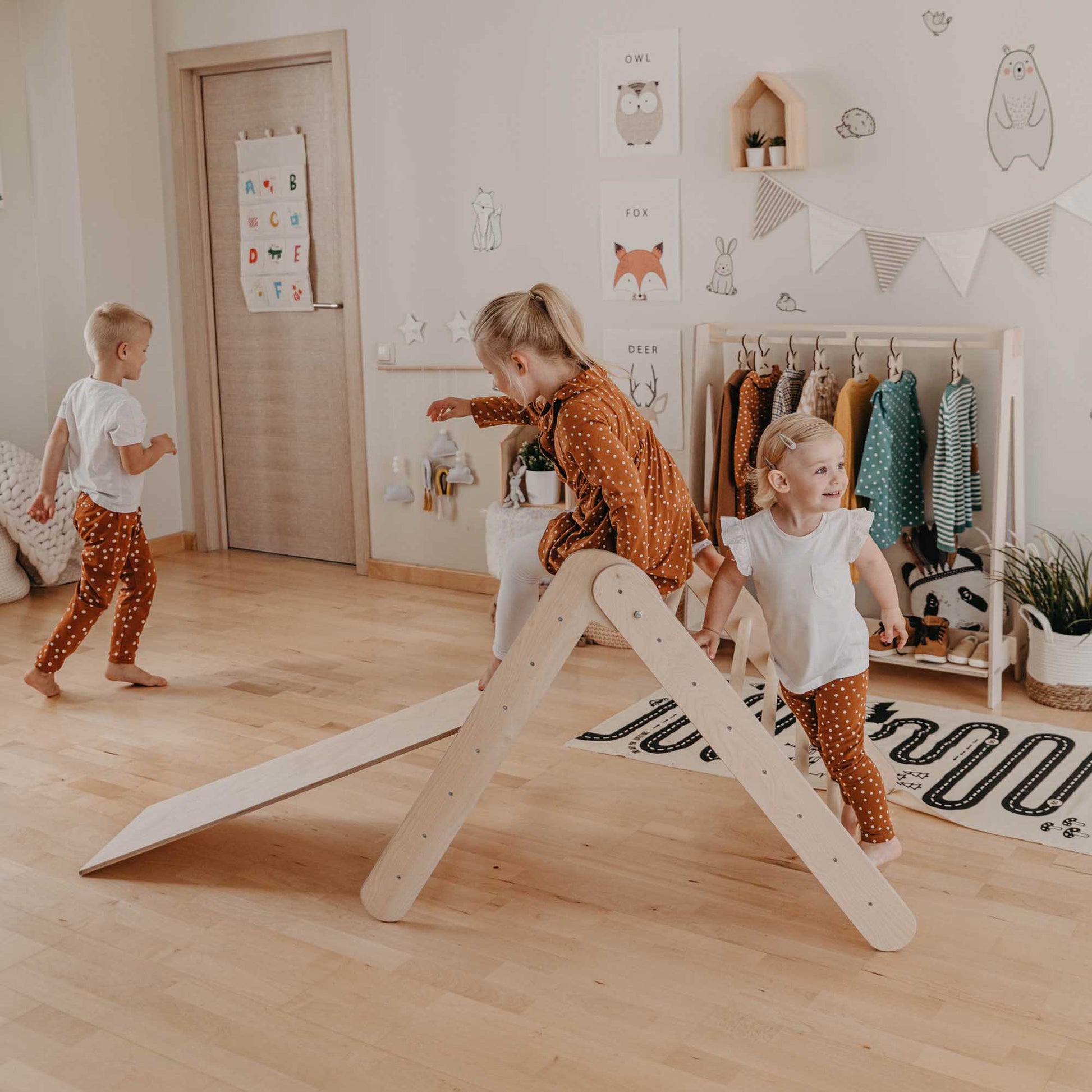 3 children playing around and on a Montessori toddler climbing triangle with a ramp.