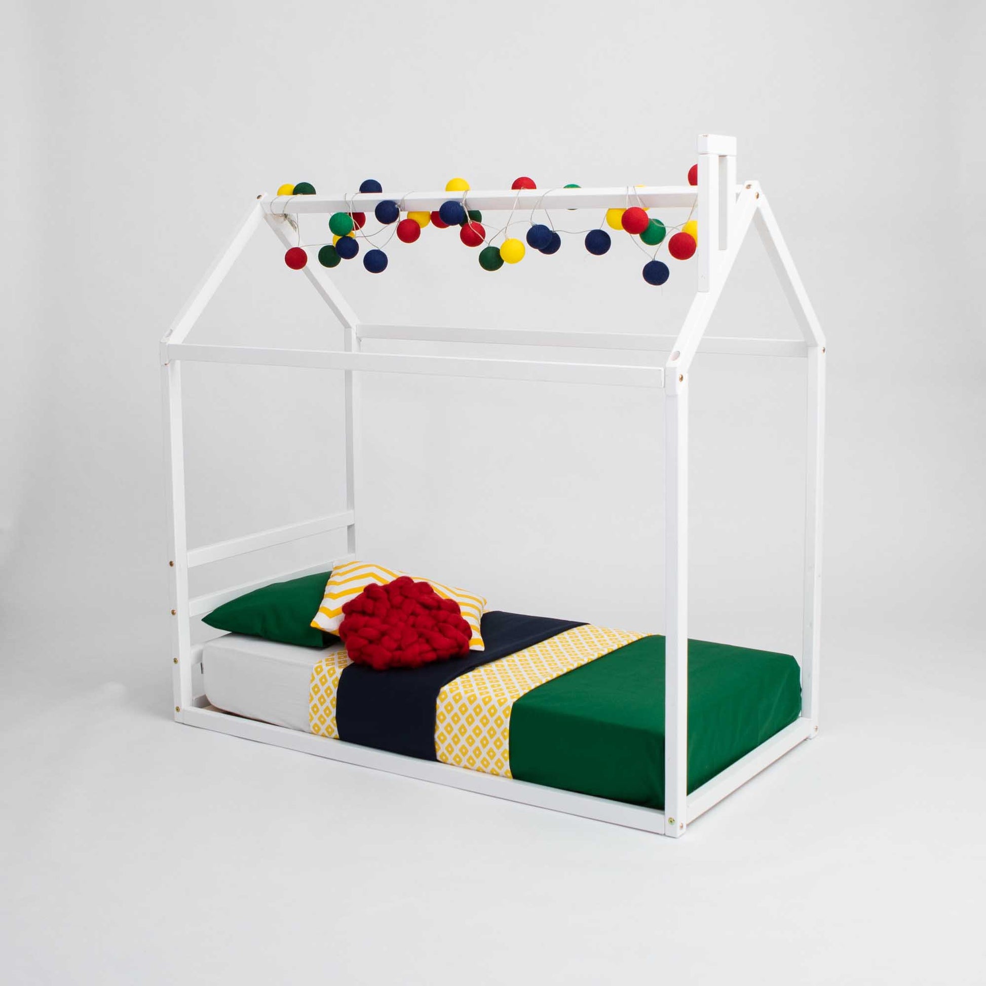 A Sweet Home From Wood children's house bed with a horizontal headboard and colorful pom poms.