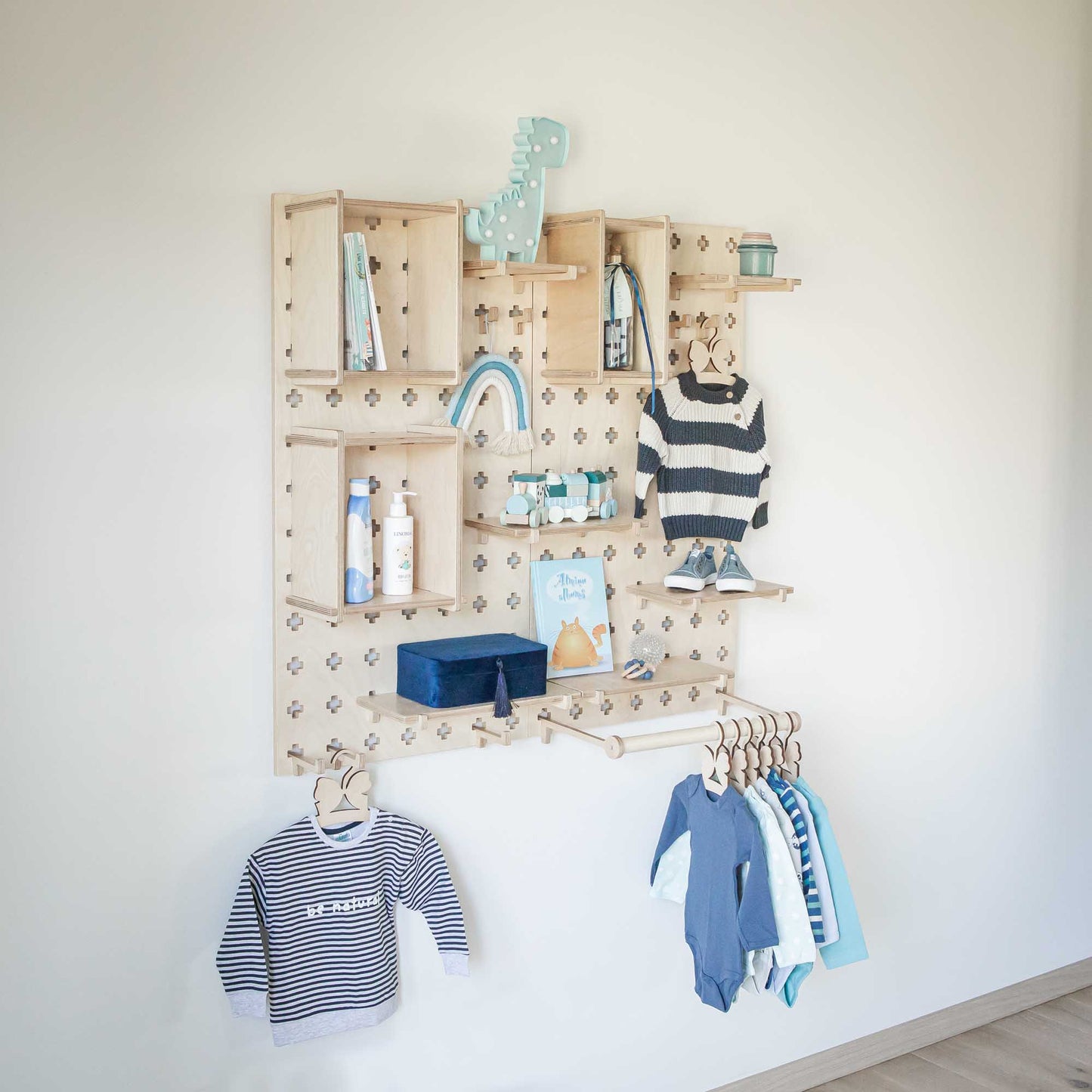 A baby room with a Large Pegboard Shelf with Clothes Hanger wall mounted with open storage shelves and montessori/floating shelves filled with clothes and toys from Sweet HOME from wood.