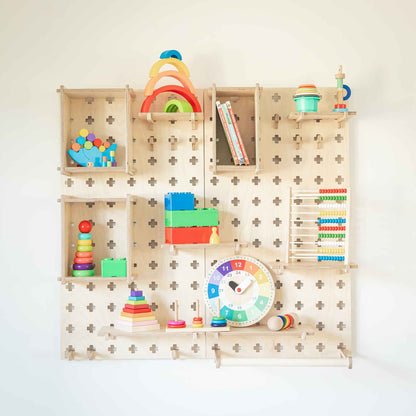 This Large Pegboard Shelf with Clothes Hanger, featuring customizable layouts, holds a delightful array of colorful children's toys, books, and a clock. The arrangement includes puzzles, stacking toys, an abacus, and a rainbow stacker on these floating shelves.