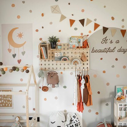 A children's room with a polka dot wall, a Pegboard with Clothes Hanger holding small plants and decor, hanging clothes, and a bed frame in the corner. An adjustable shelves organizer provides extra storage space, while a banner and the phrase "It's a beautiful day" adorn the wall.