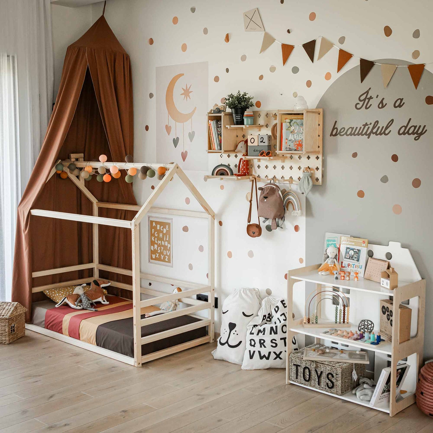 A children's bedroom with a house-shaped bed, toys, a play kitchen, a canopy, wall decorations, and an "It's a beautiful day" sign. Decor includes bunting, polka dots, and a wooden shelf with books and plants. A versatile Pegboard Wall Shelf offers expandable options for organizing toys and crafts.