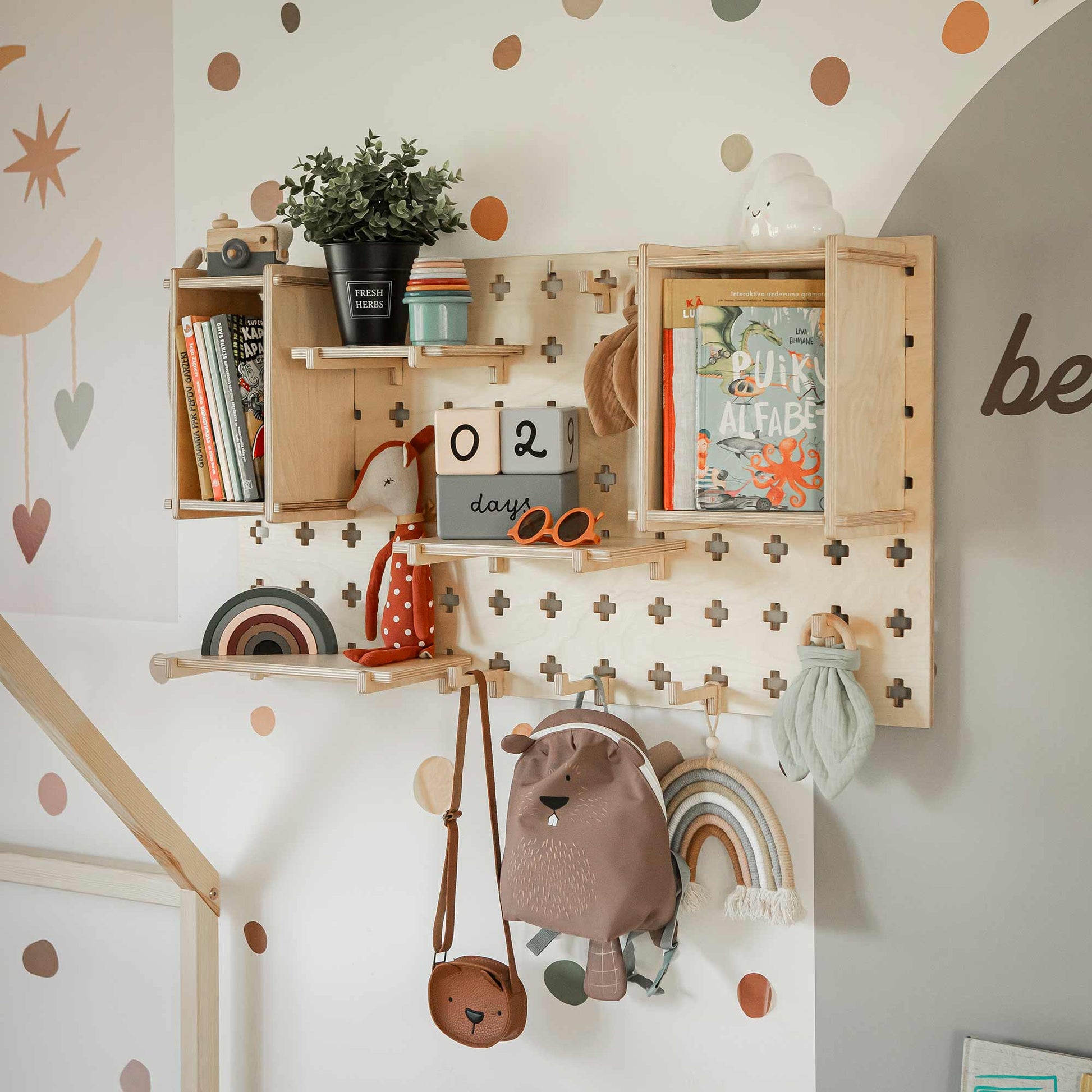 A Pegboard Wall Shelf with books, a plant, a calendar displaying '02 days,' a pair of glasses, small containers, a stuffed mushroom, a bear-themed backpack, and rainbow decorations offers versatile storage solutions.