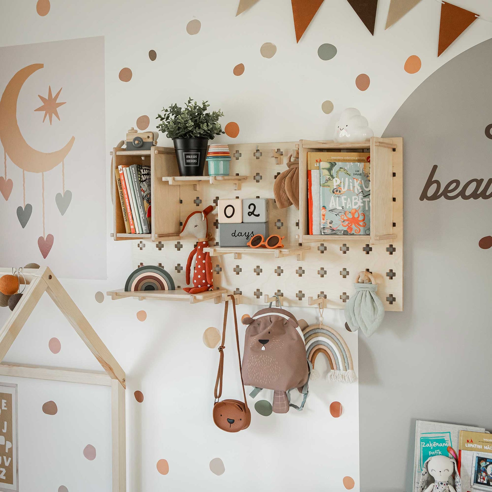 A children's room featuring wall-mounted shelves holding books and decor, a versatile Pegboard Wall Shelf with expandable options for organizing toys, a calendar showing "02 day," colorful buntings, polka dot wall stickers, and playful items like a hanging backpack and a stuffed toy.